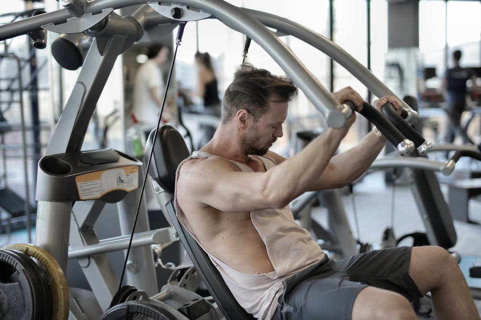 Side view of concentrated male athlete in sportswear pumping muscles during training in fitness center and using shoulder press machine