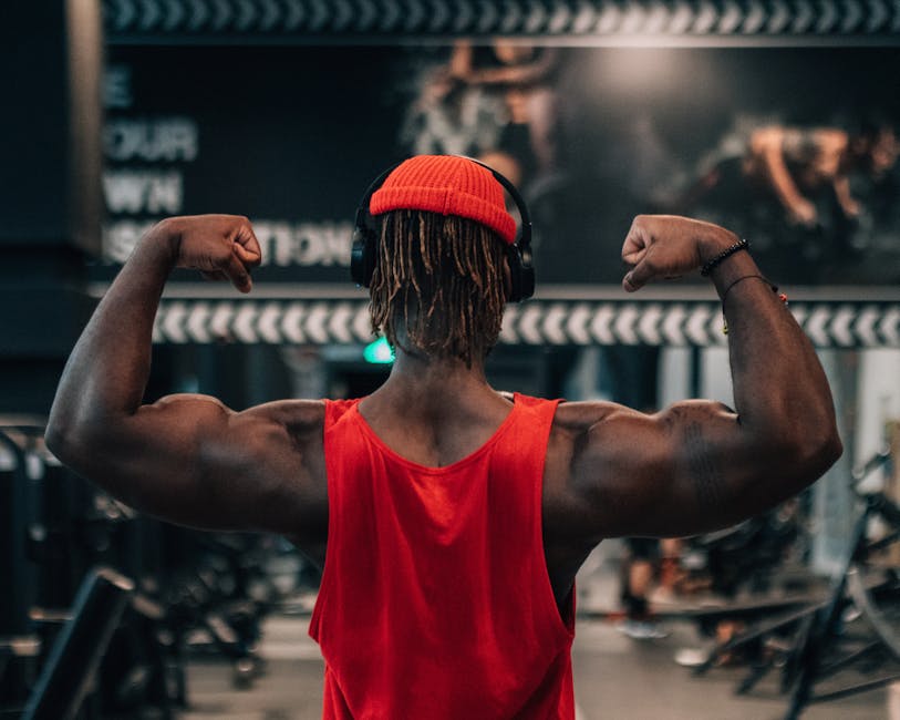 A man in a red tank top flexing his arm muscles in a gym setting, conveying motivation and strength.