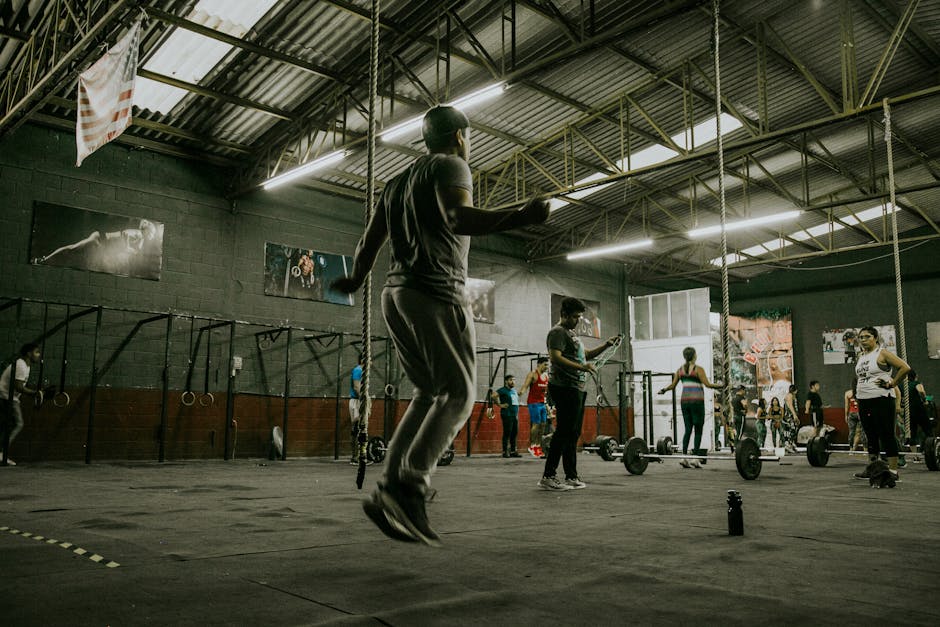 Dynamic CrossFit session with multiple adults exercising indoors using various equipment.