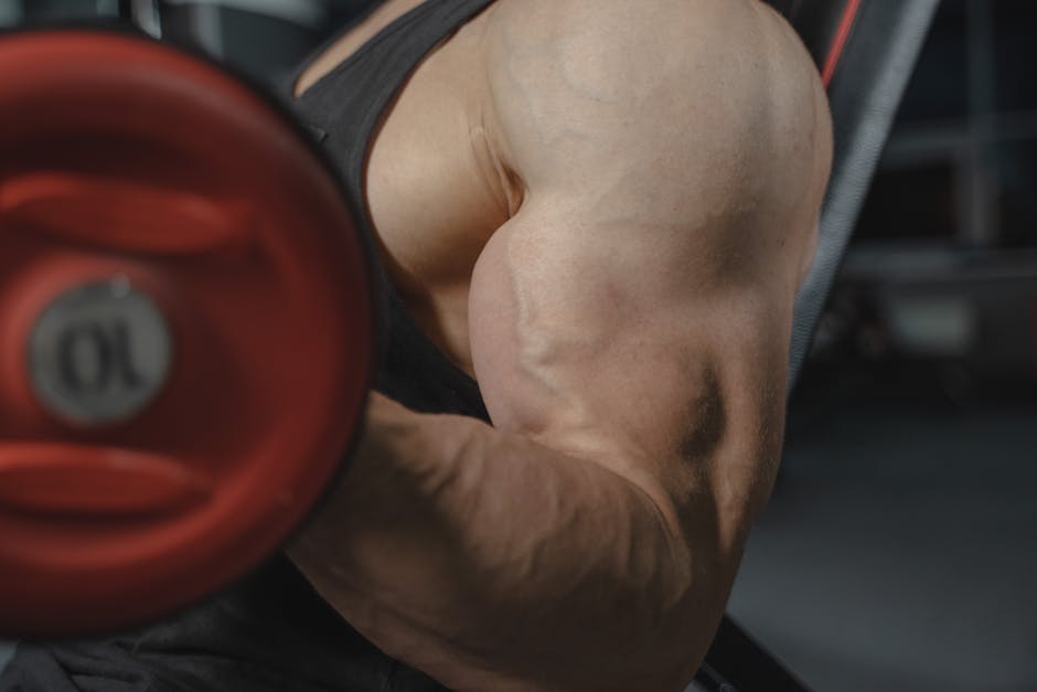A focused view of a bodybuilder's arm muscles lifting a dumbbell in a gym setting.