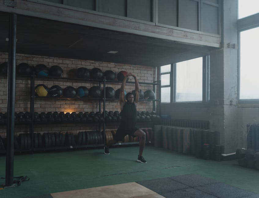 A man performing stretches in a spacious, well-equipped industrial gym environment